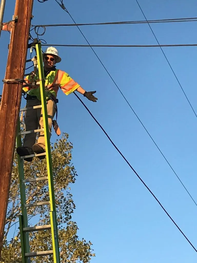 Diana Olivas stands at the top of a ladder leaning on a telephone pole.